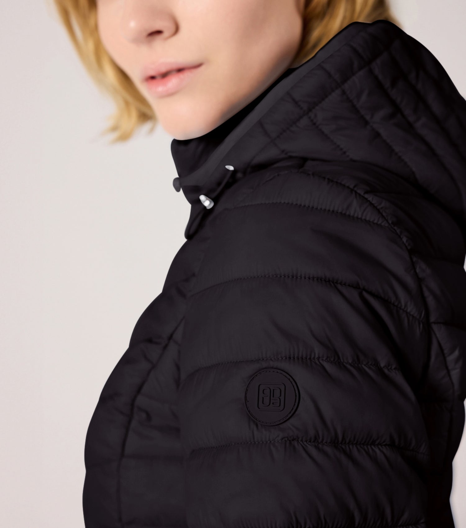 Frau mit Schwarzer Steppjacke und weißem T-shirt. Modell ist 177cm groß und trägt Größe 36.
