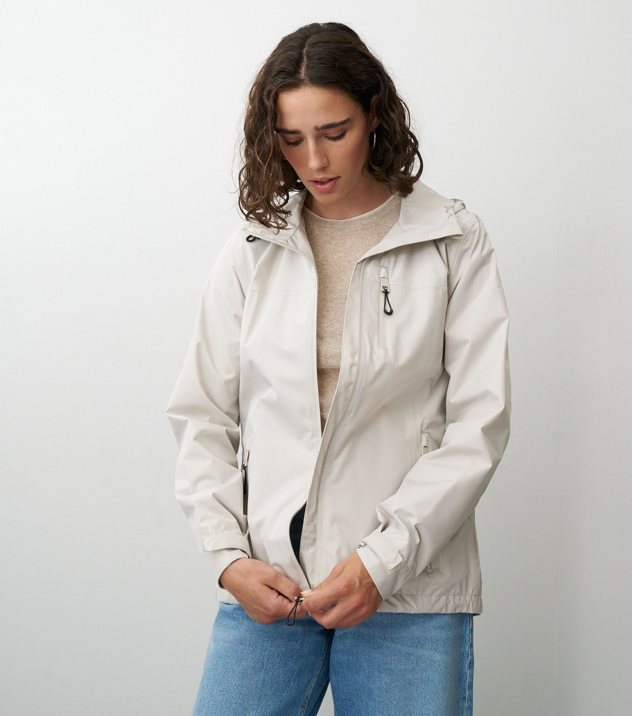 Braunhaarige Frau die frontal zur Kamera steht und eine beige Regenjacke schließt