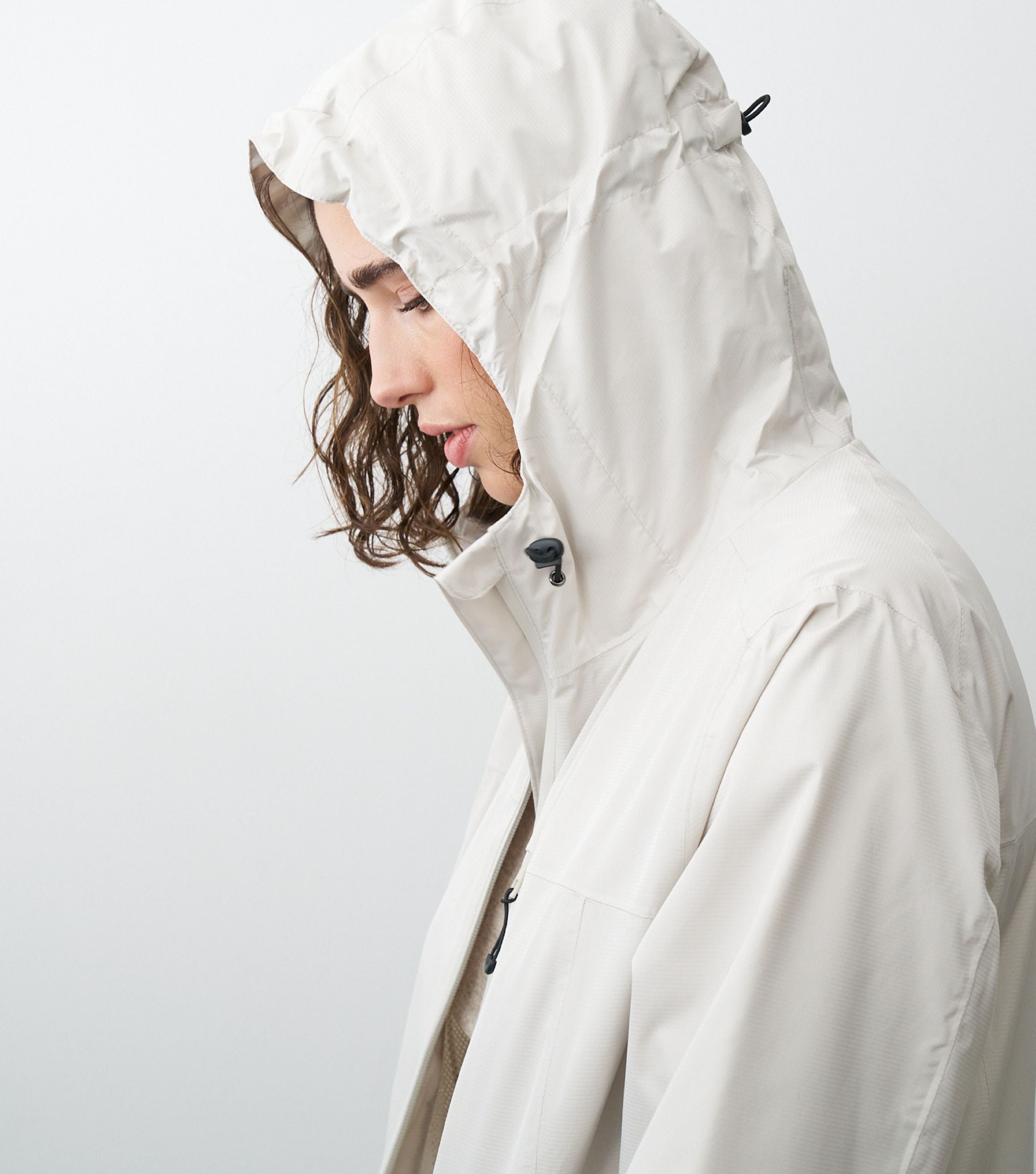 Seitliche Ansicht einer Frau die eine beige Regenjacke trägt und die Kapuze aufhat
