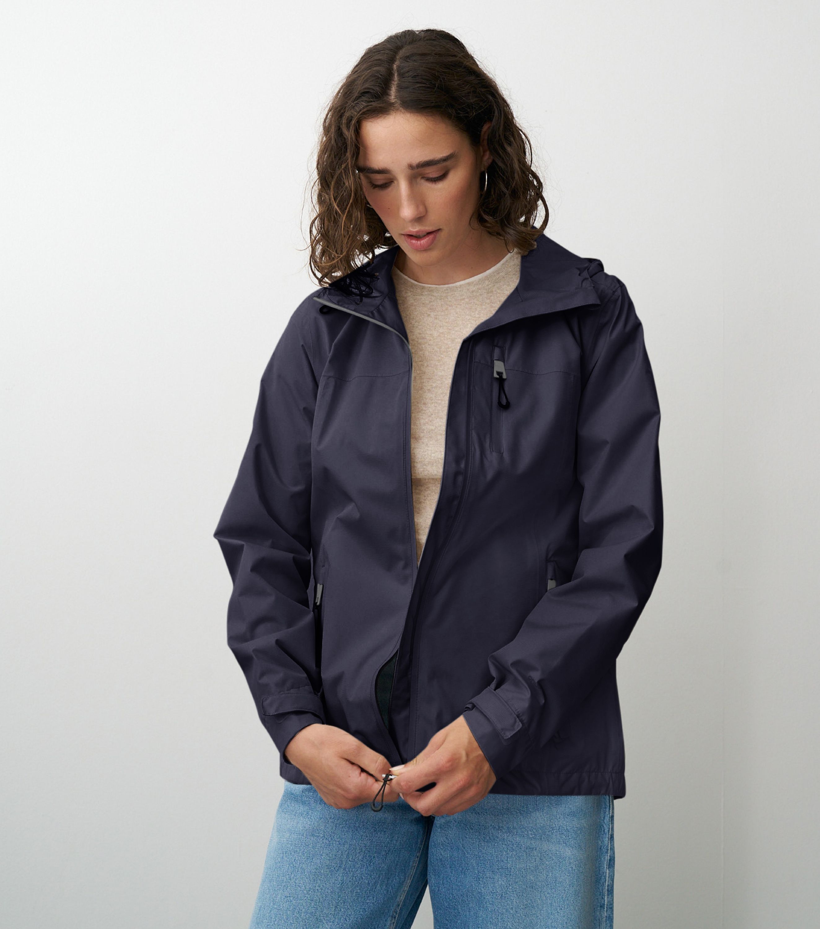 Braunhaarige Frau die frontal zur Kamera steht und eine blaue Regenjacke schließt