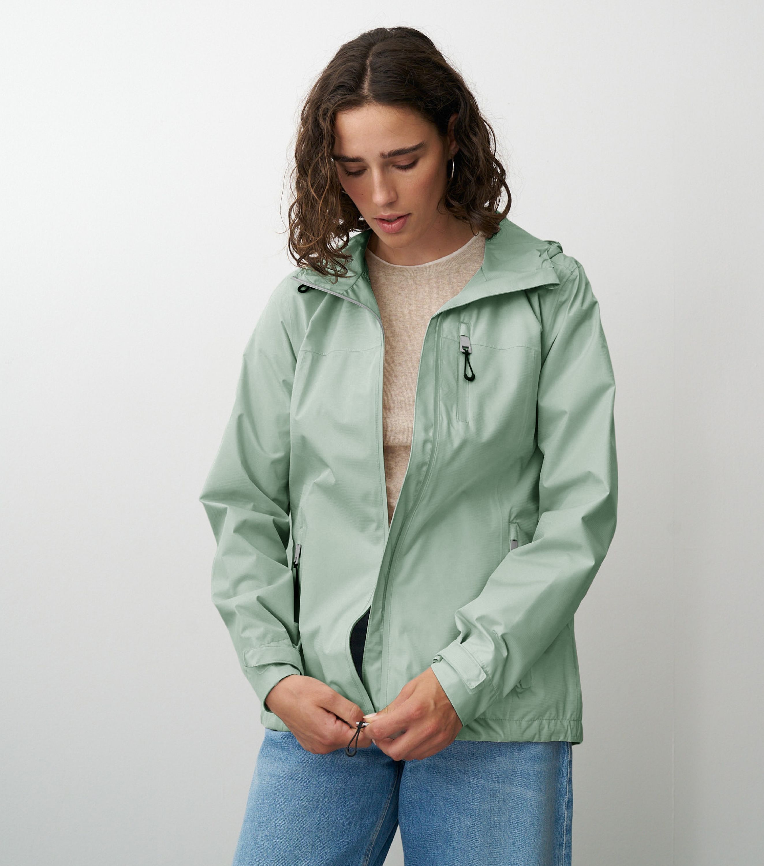 Braunhaarige Frau die frontal zur Kamera steht und eine grüne Regenjacke schließt