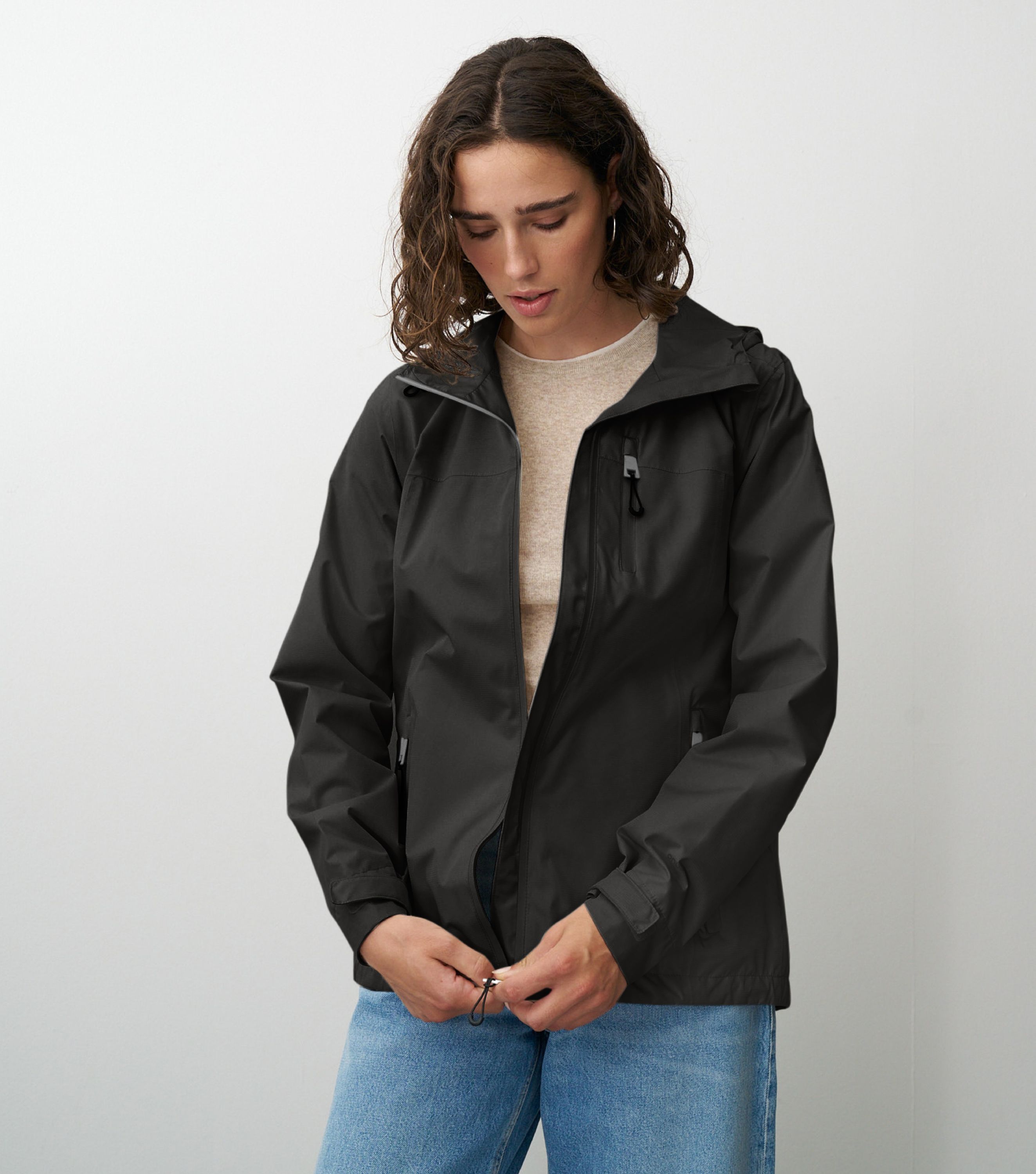 Braunhaarige Frau die frontal zur Kamera steht und eine schwarze Regenjacke schließt