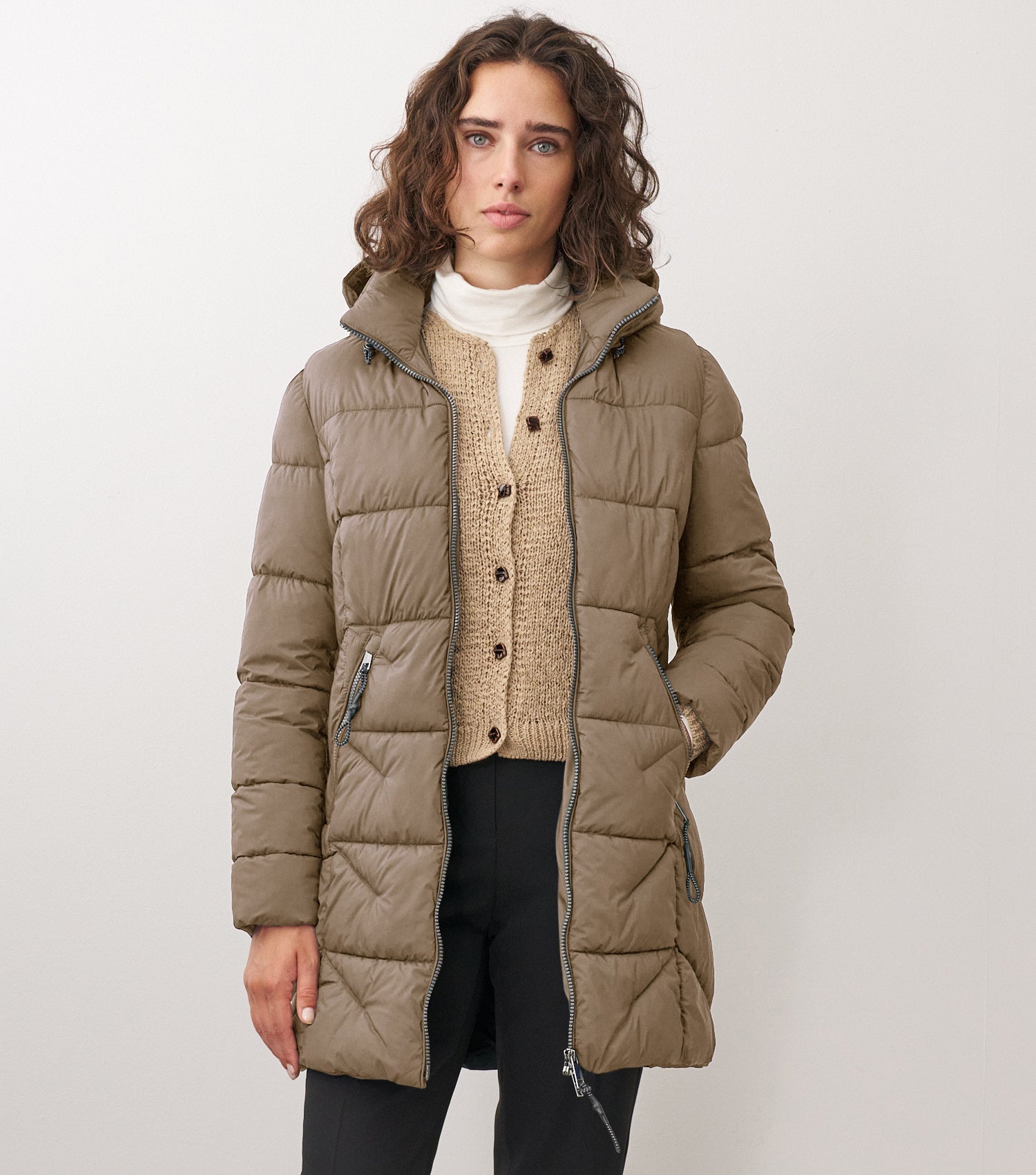 Braunhaarige Frau steht frontal zur Kamera mit blauer Winterjacke und beigem Sweater drunter