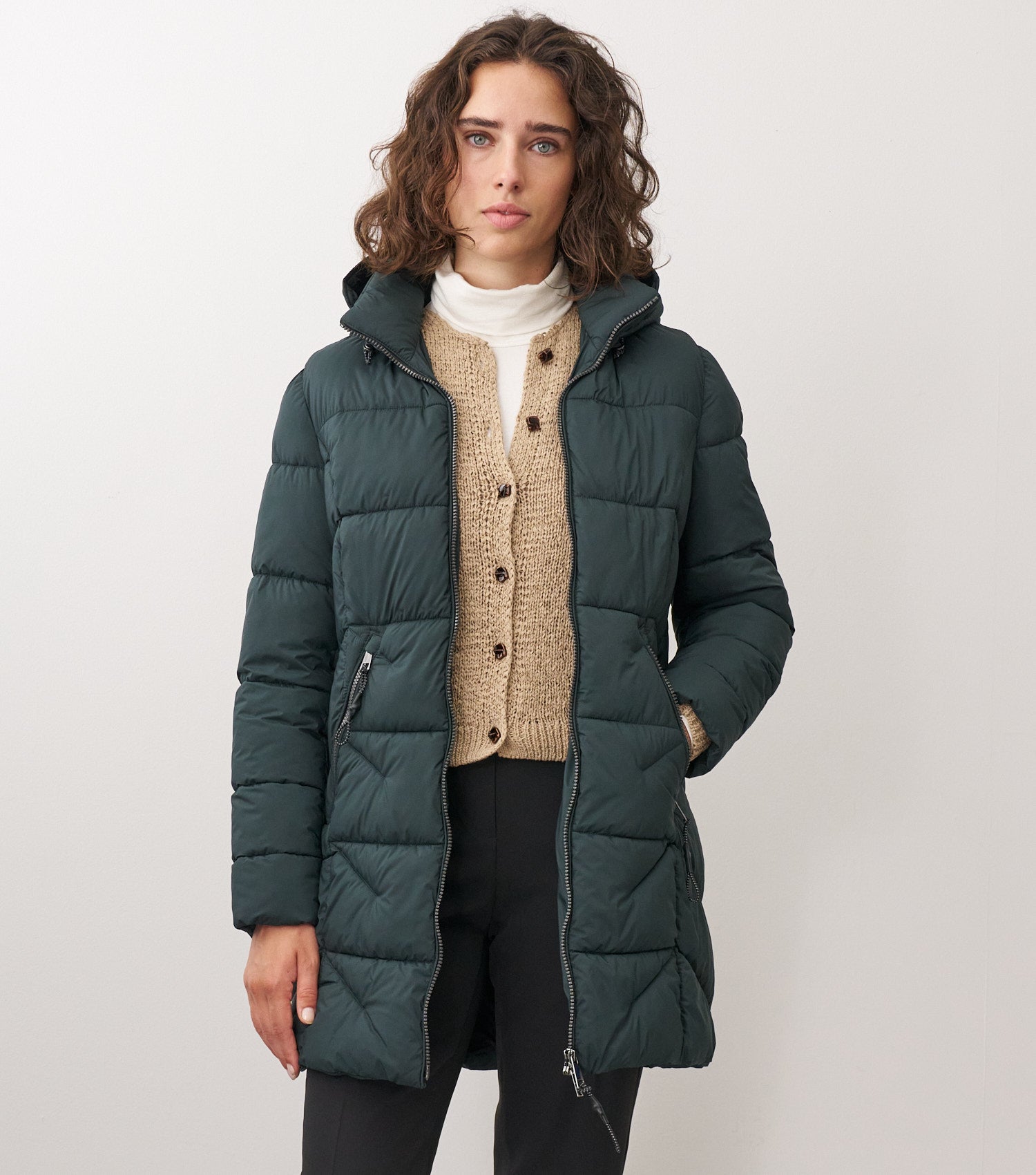 Braunhaariges Model trägt dunkelgrüne Winterjacke über einem beigen Cardigan