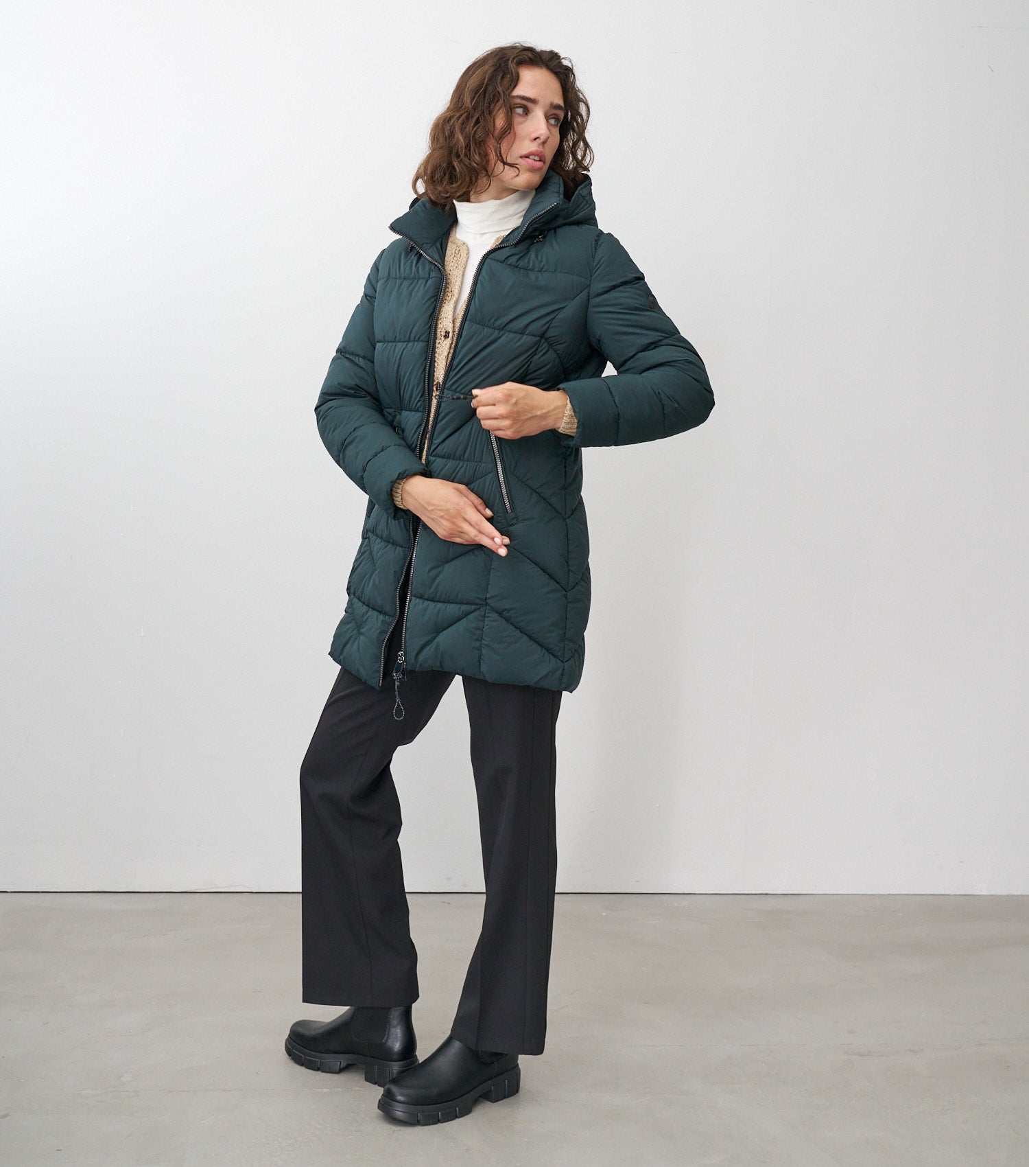 Ganzkörperansicht eines braunhaarigen Models, die eine dunkelgrüne Winterjacke trägt