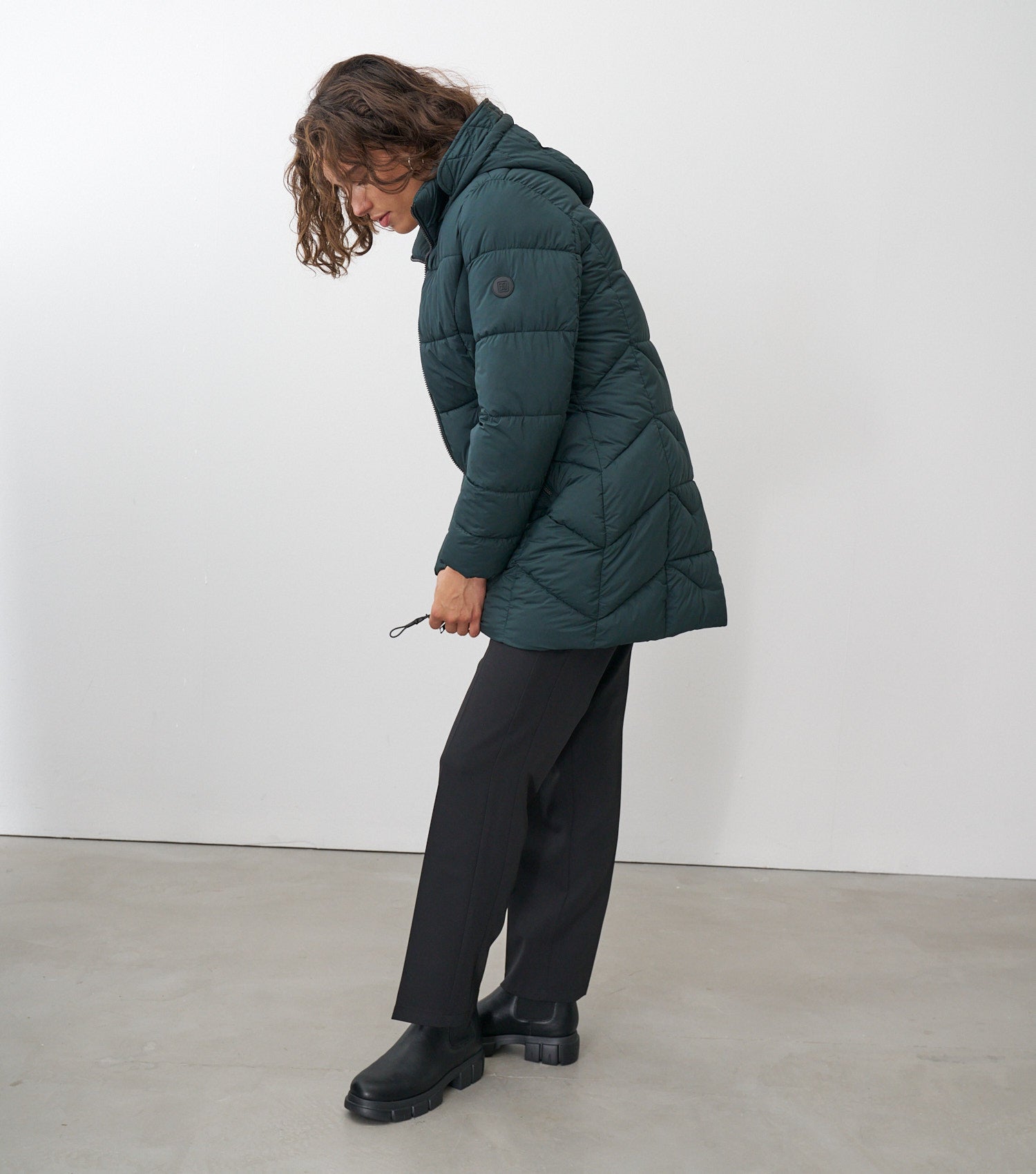 Seitenansicht eines braunhaarigen Models, die eine dunkelgrüne Winterjacke trägt