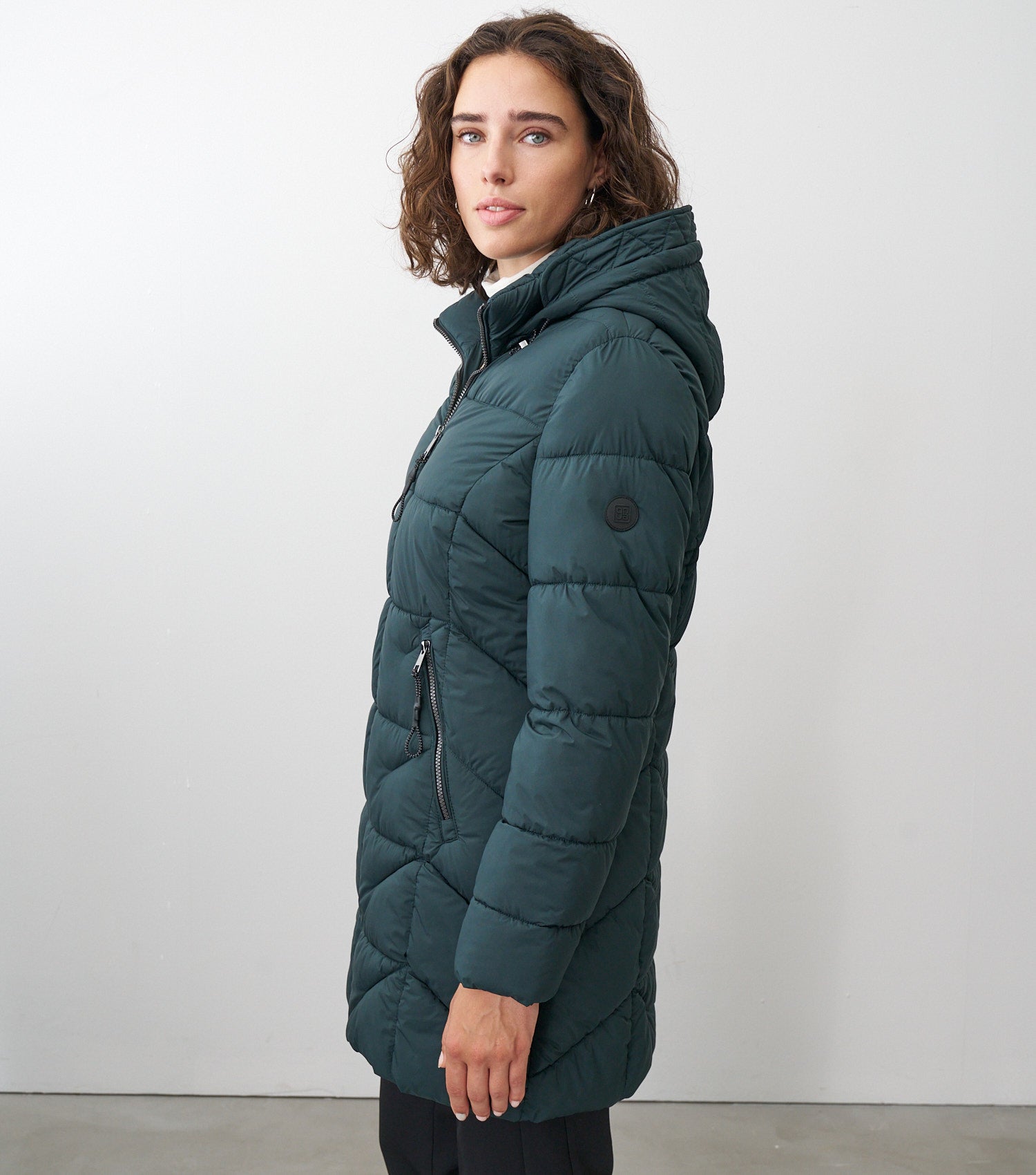 Seitenansicht eines braunhaarigen Models, die eine dunkelgrüne Winterjacke trägt