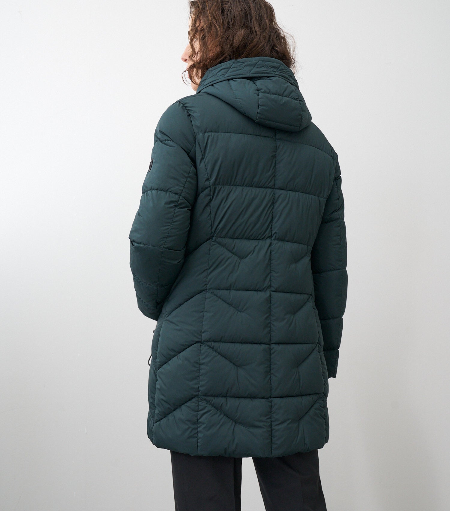 Rückansicht eines braunhaarigen Models, die eine dunkelgrüne Winterjacke trägt