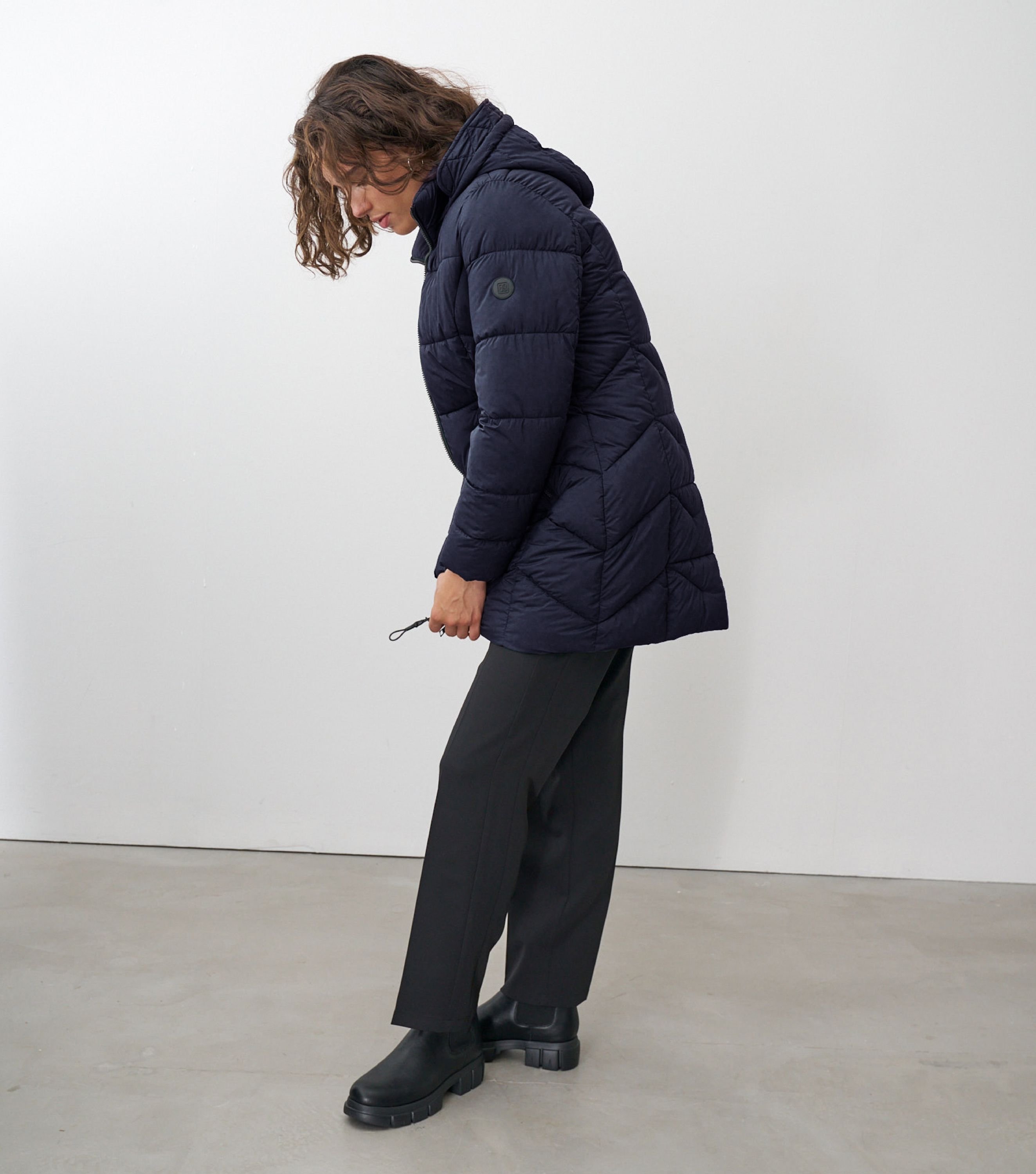 Seitliche Ansicht einer braunhaarigen Frau wie sie eine grüne Winterjacke schließt