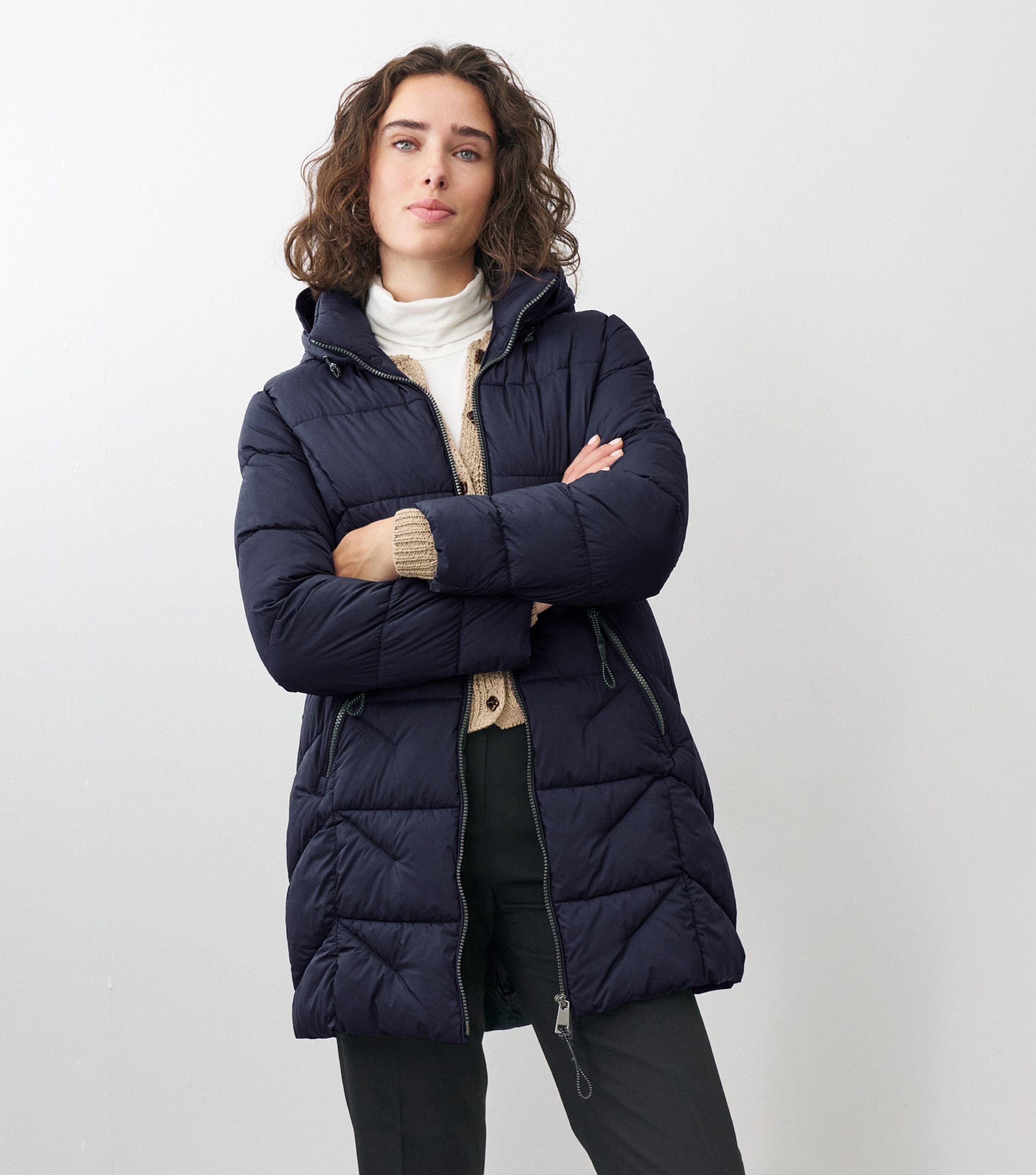 Braunhaarige Frau steht frontal zur Kamera mit verschränkten Armen mit blauer Winterjacke