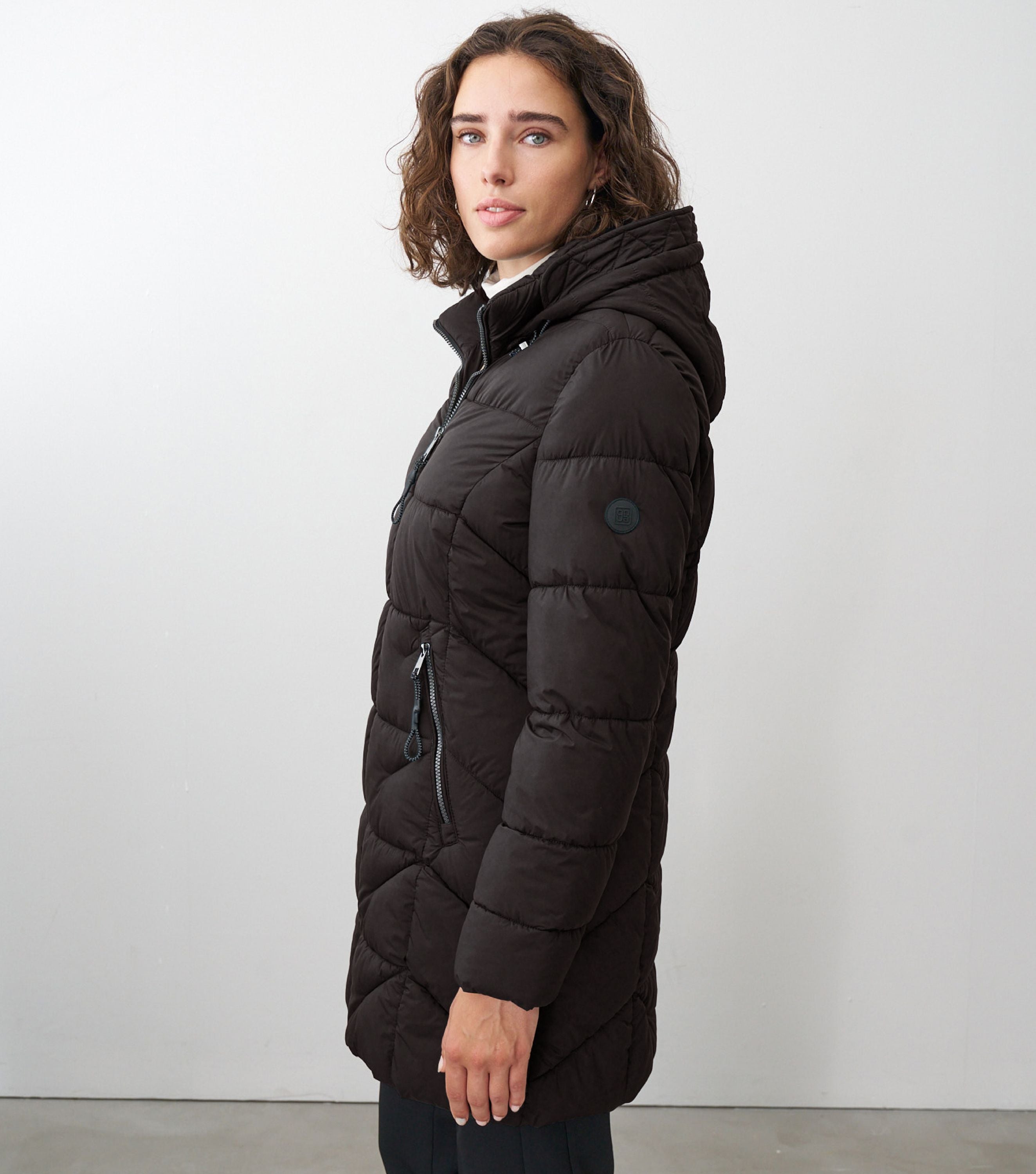 Braunhaarige Frau steht seitlich zur Kamera mit schwarzer Winterjacke