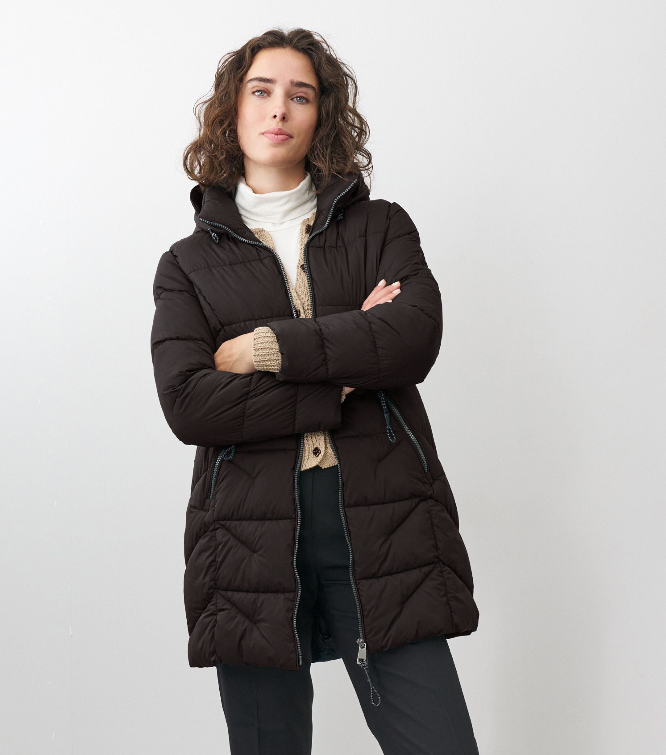 Braunhaarige Frau steht frontal zur Kamera mit verschränkten Armen mit schwarzen Winterjacke