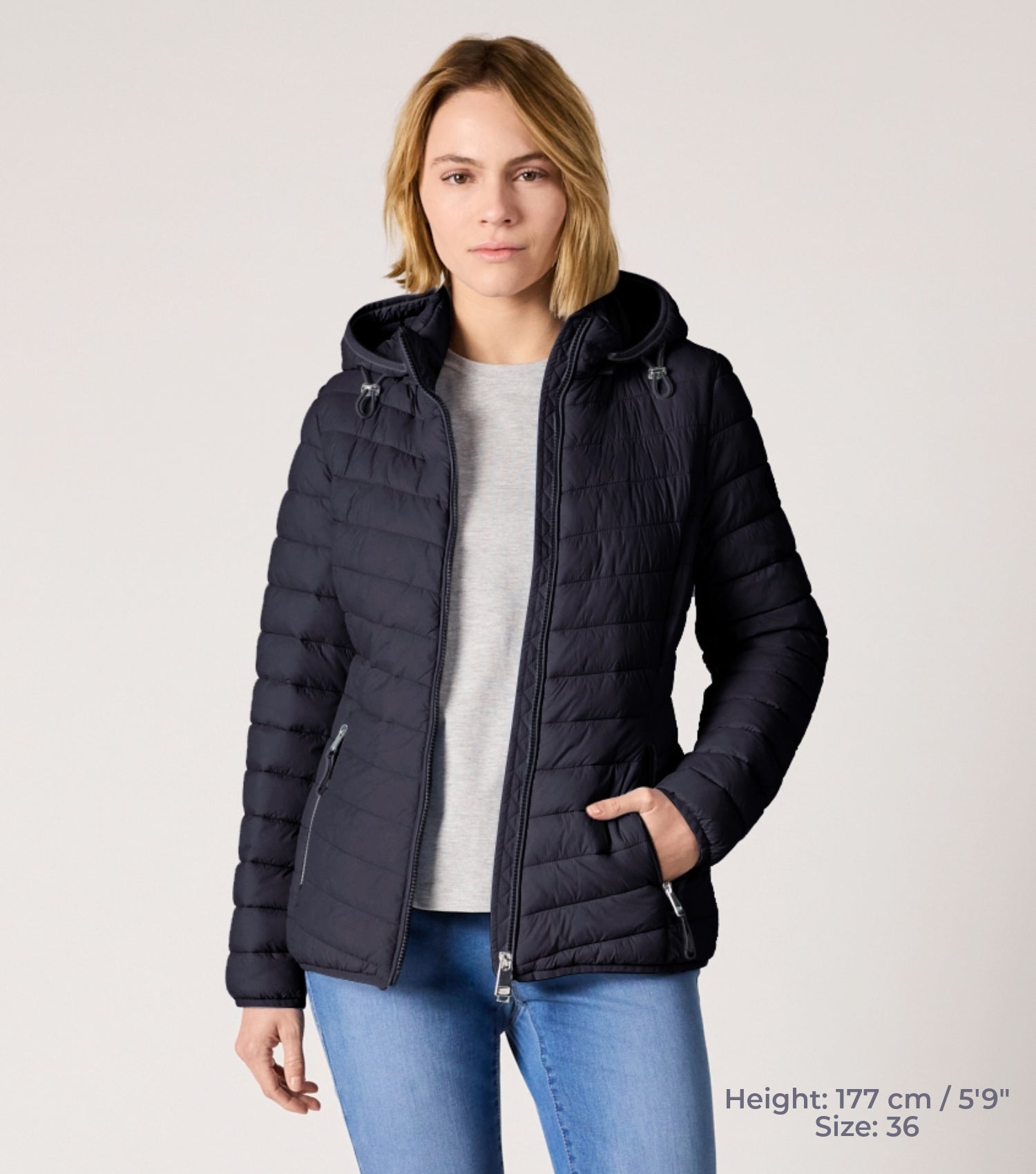 Frau mit blauer Steppjacke und weißem T-shirt. Modell ist 177cm groß und trägt Größe 36. 