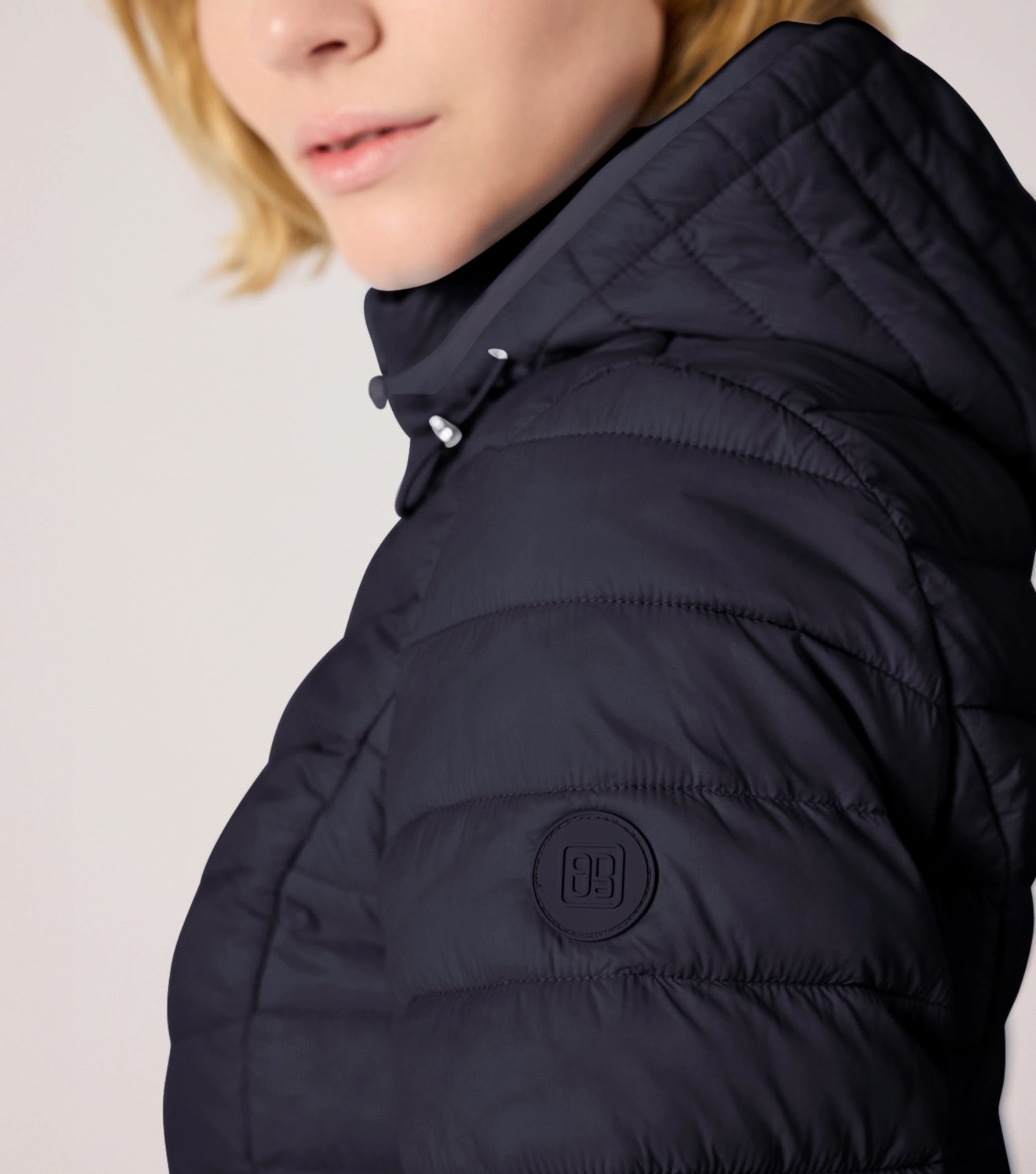 Frau mit blauer Steppjacke und weißem T-shirt. Modell ist 177cm groß und trägt Größe 36. 