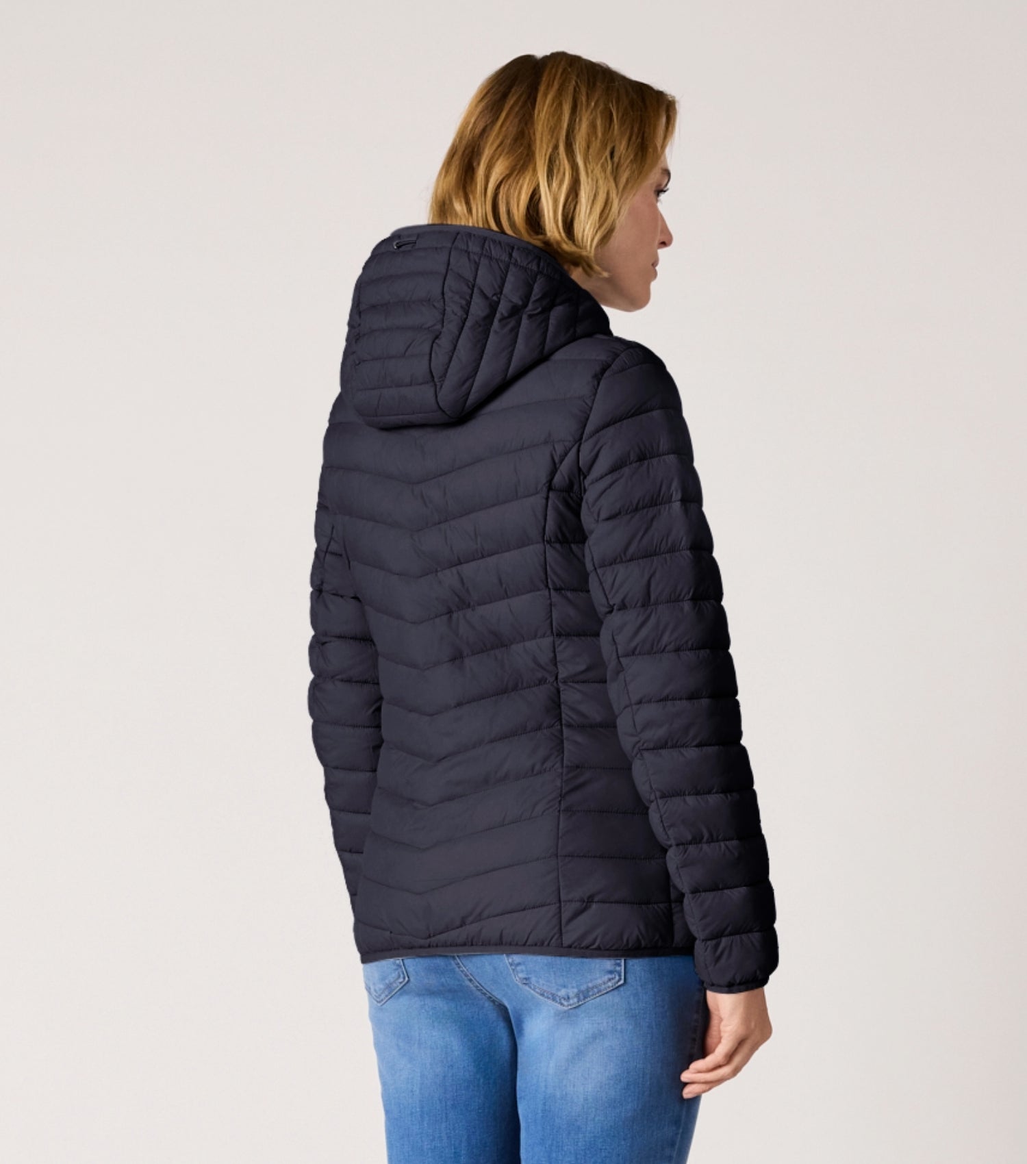 Rückansicht Frau mit blauer Steppjacke und weißem T-shirt. 