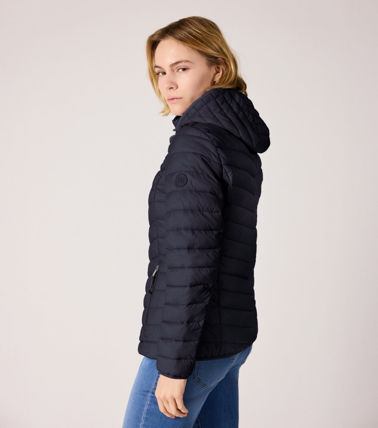 Seitenansicht Frau mit blauer Steppjacke und weißem T-shirt. 