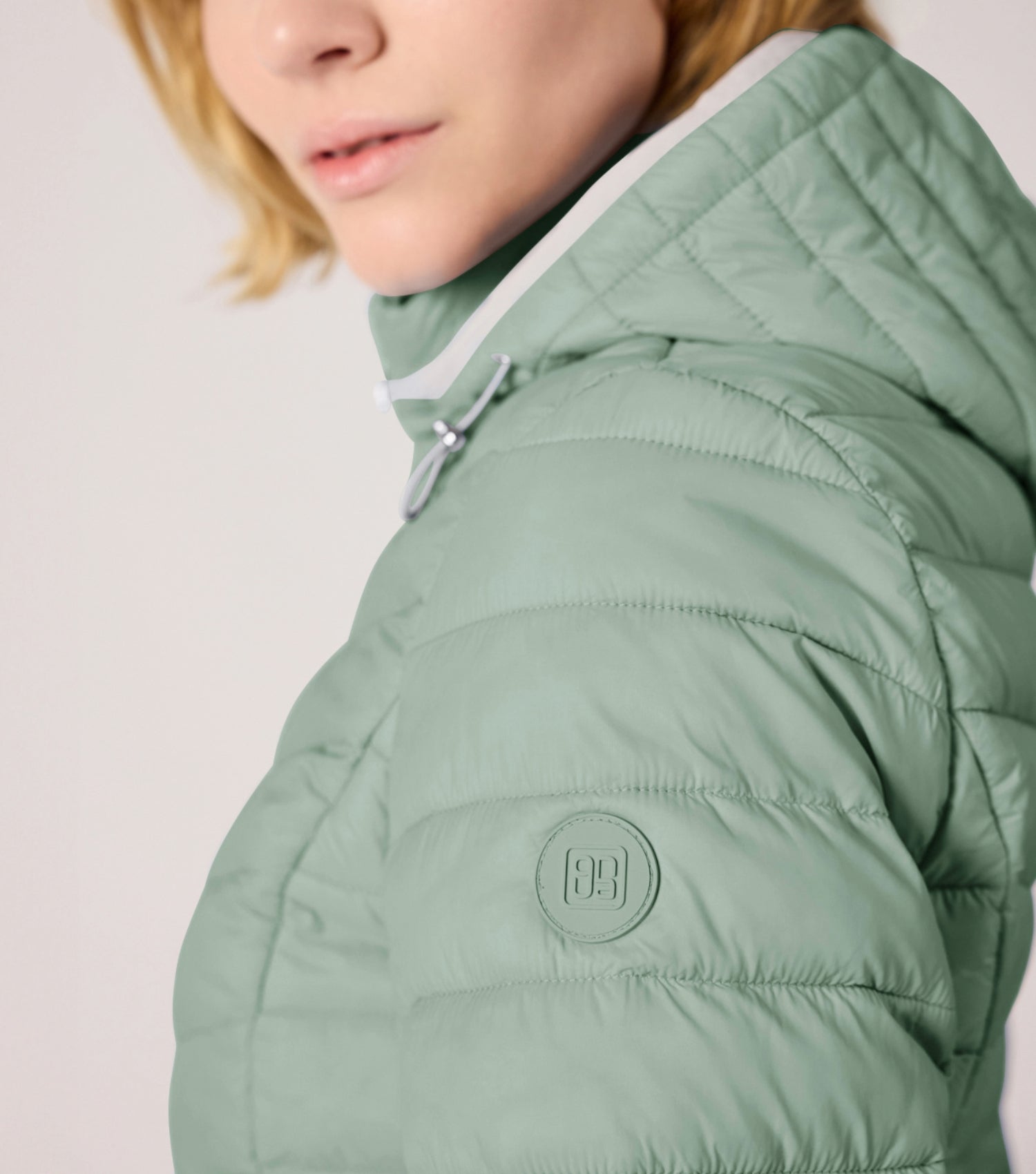 Frau mit grüner Steppjacke und weißem T-shirt. Modell ist 177cm groß und trägt Größe 36. 