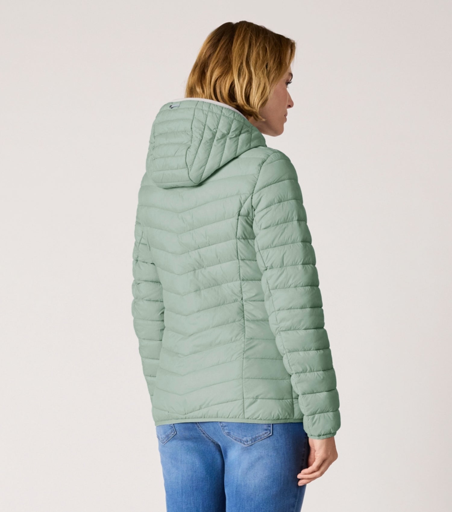 Rückansicht Frau mit grüner Steppjacke und weißem T-shirt. 