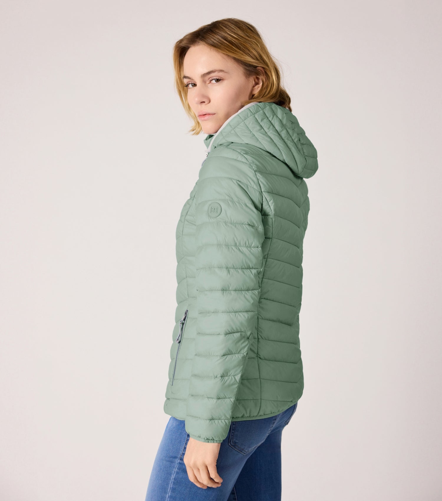 Seitenansicht Frau mit grüner Steppjacke und weißem T-shirt.  