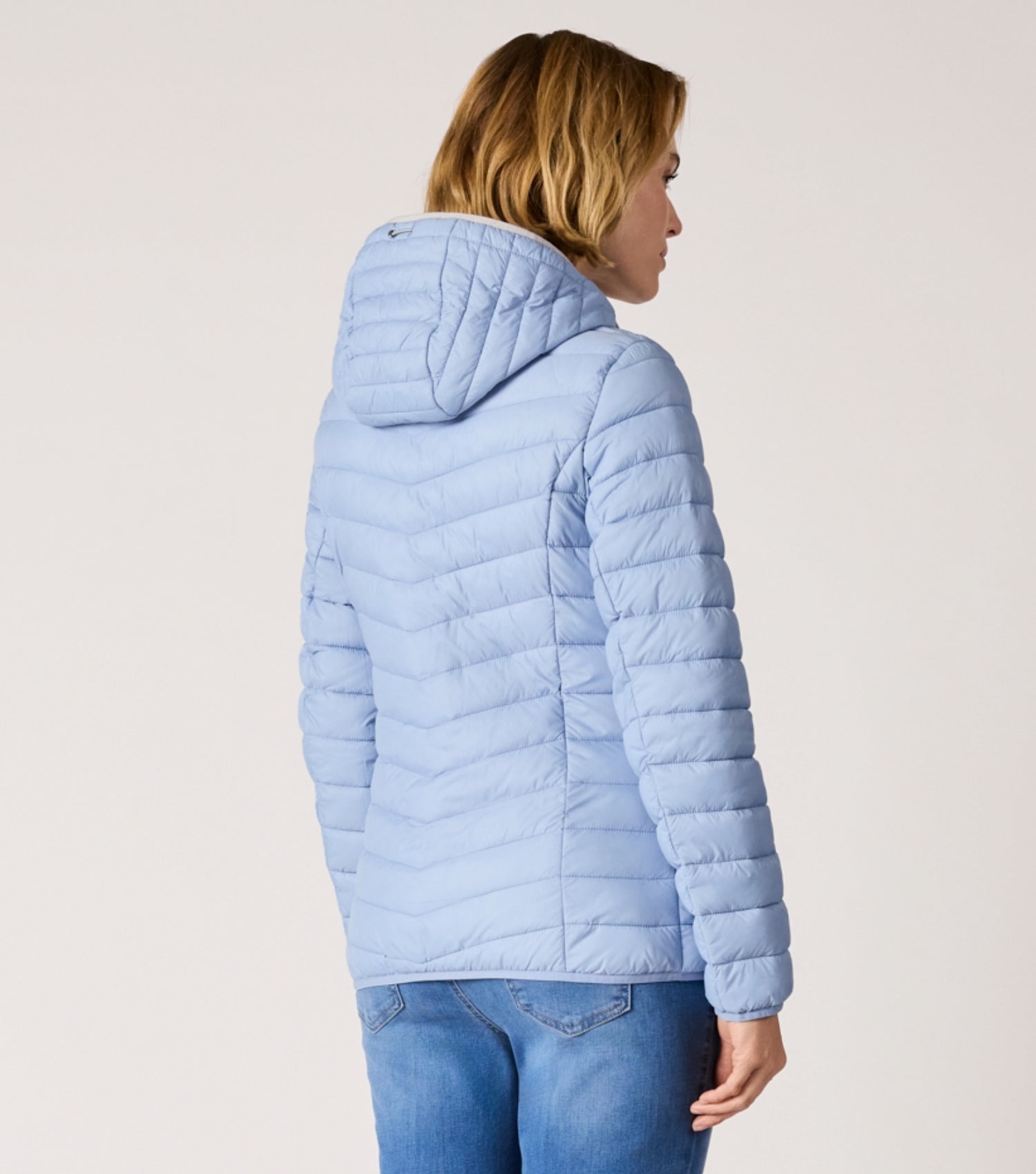 Rückansicht Frau mit blauer Steppjacke und weißem T-shirt. 