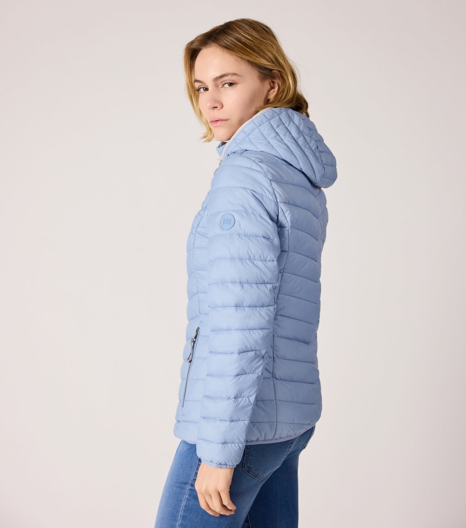 Seitenansicht Frau mit blauer Steppjacke und weißem T-shirt. 