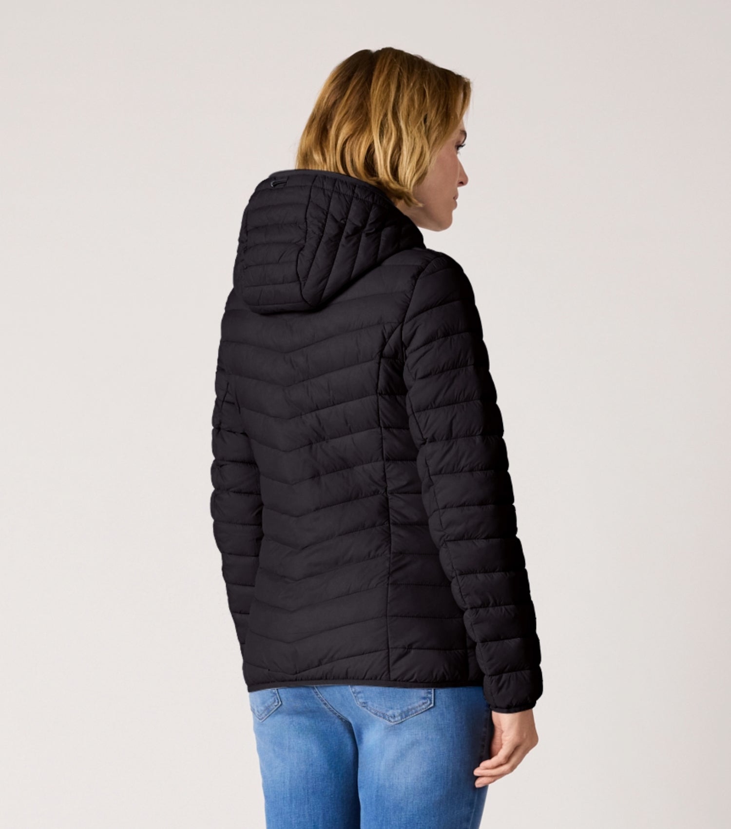 Rückansicht Frau mit schwarzer Steppjacke und weißem T-shirt. 