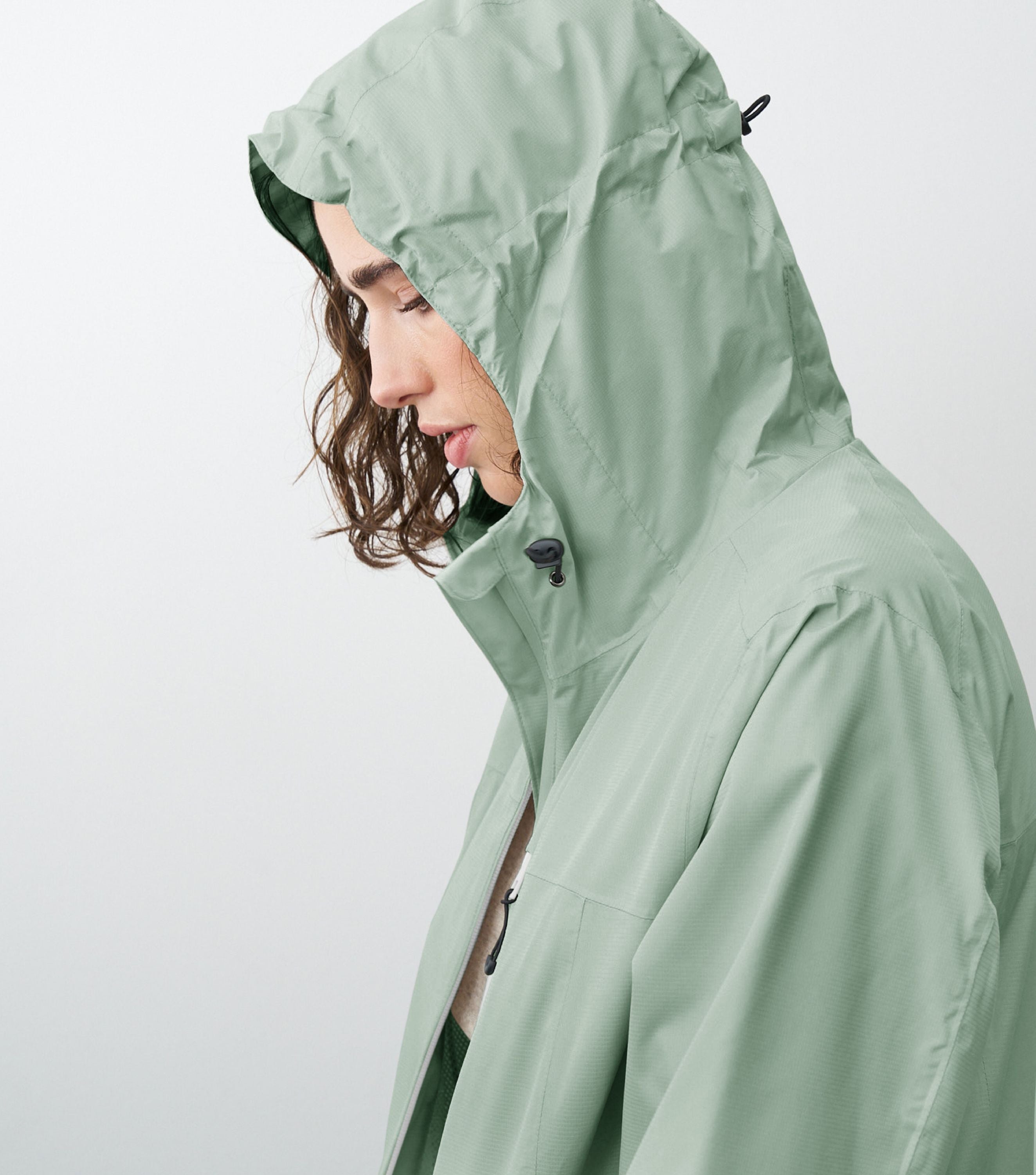 Seitliche Ansicht einer Frau die eine grüne Regenjacke trägt und die Kapuze aufhat 