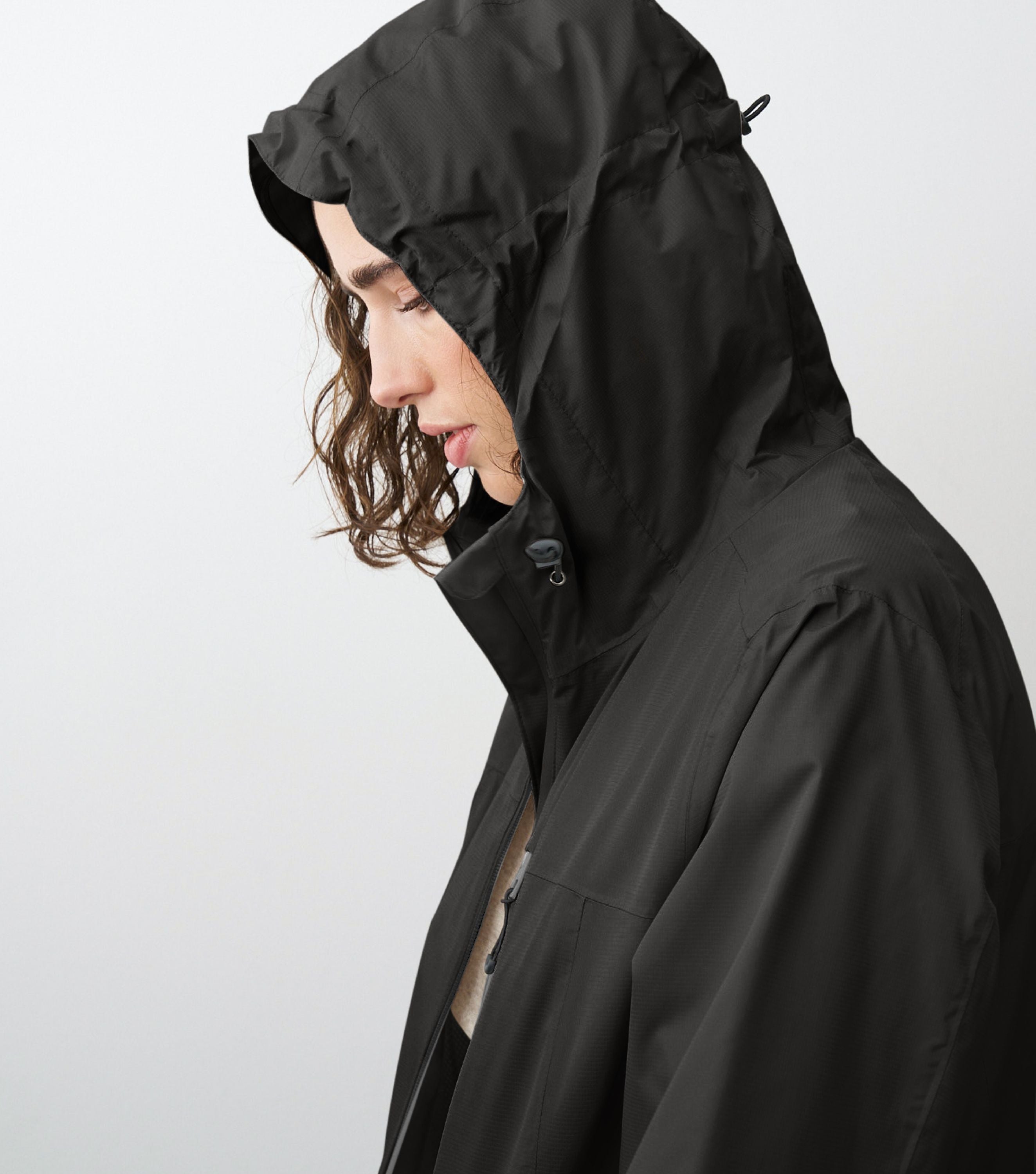 Seitliche Ansicht einer Frau die eine schwarze Regenjacke trägt und die Kapuze aufhat 