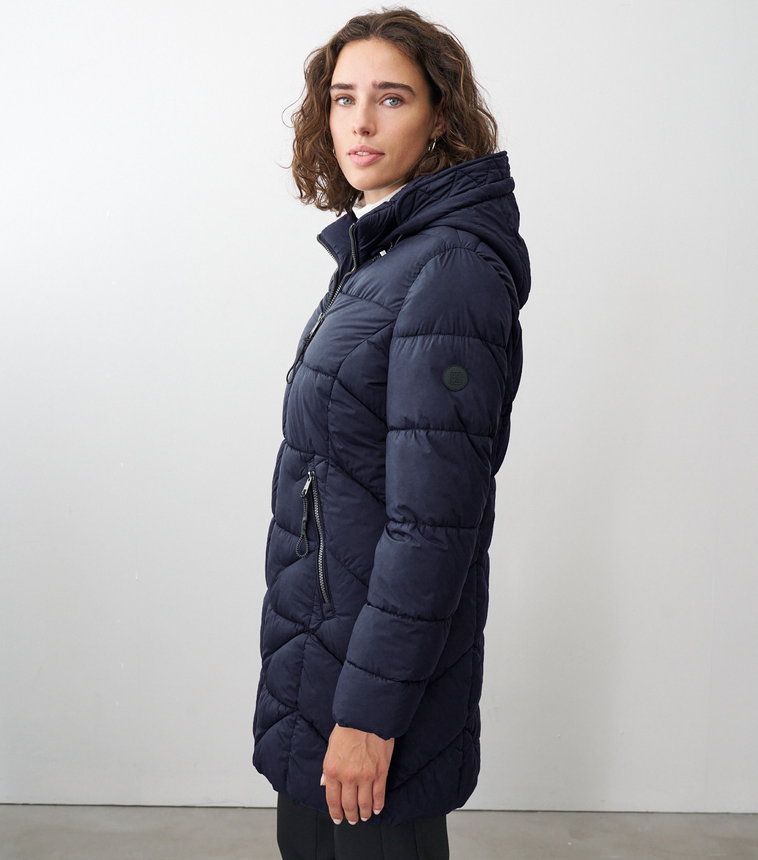Braunhaarige Frau steht seitlich zur Kamera mit blauer Winterjacke 